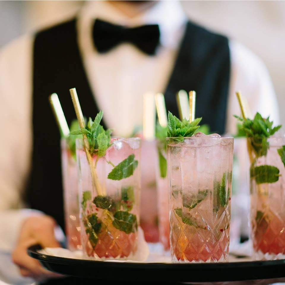 A waiter in a bow tie and waistcoat serving a tray of cocktails