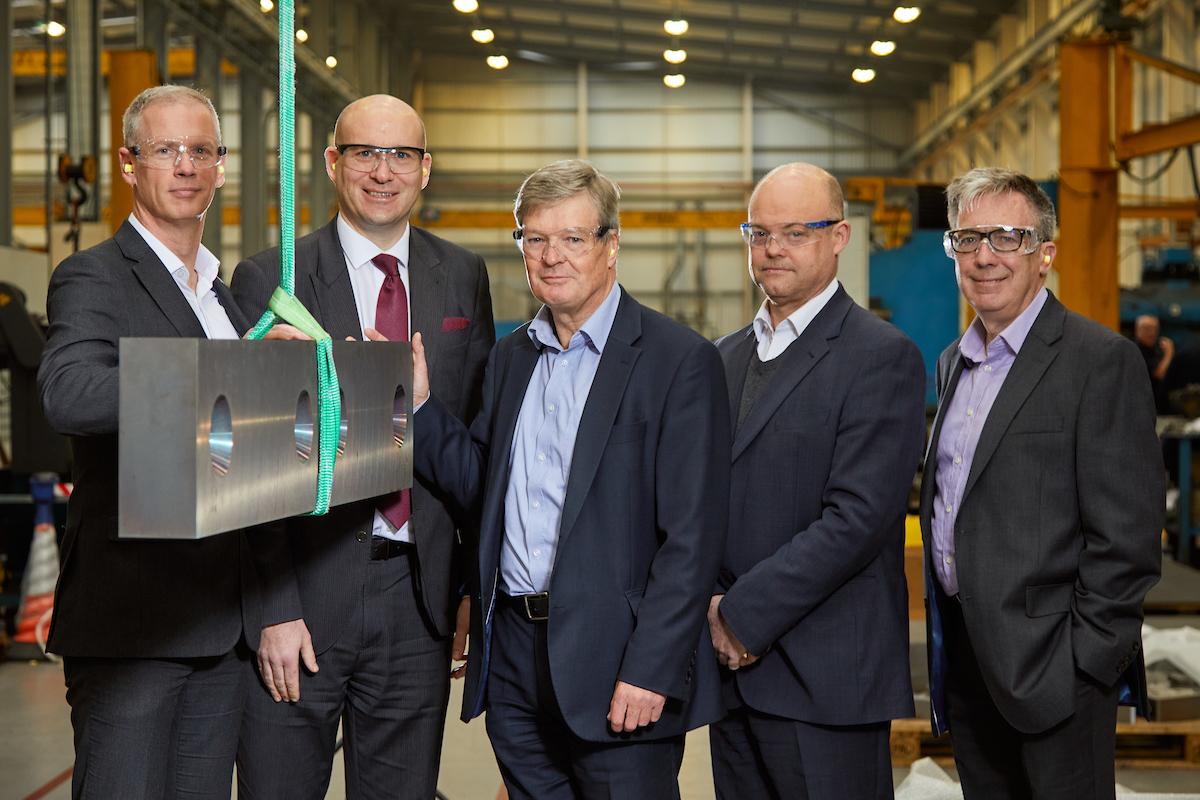 Five men in suits wearing protective goggles standing in a suspension parts factory