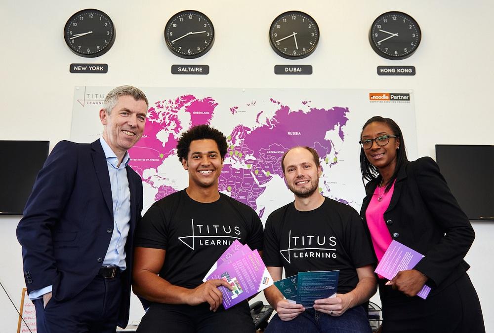 Four employees from Titus Learning standing in front of a world map and clocks
