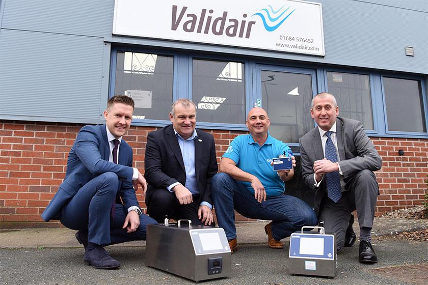 Four men kneeling in front of the Validair office showing their environmental monitoring equipment