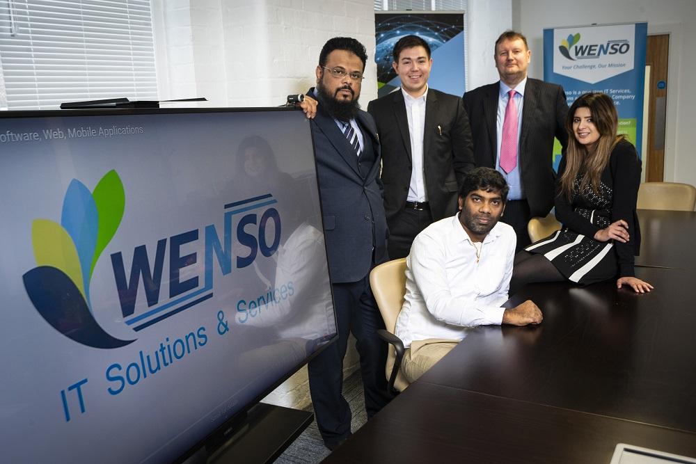 A group of employees from Wenso standing around a table and next to a TV screen