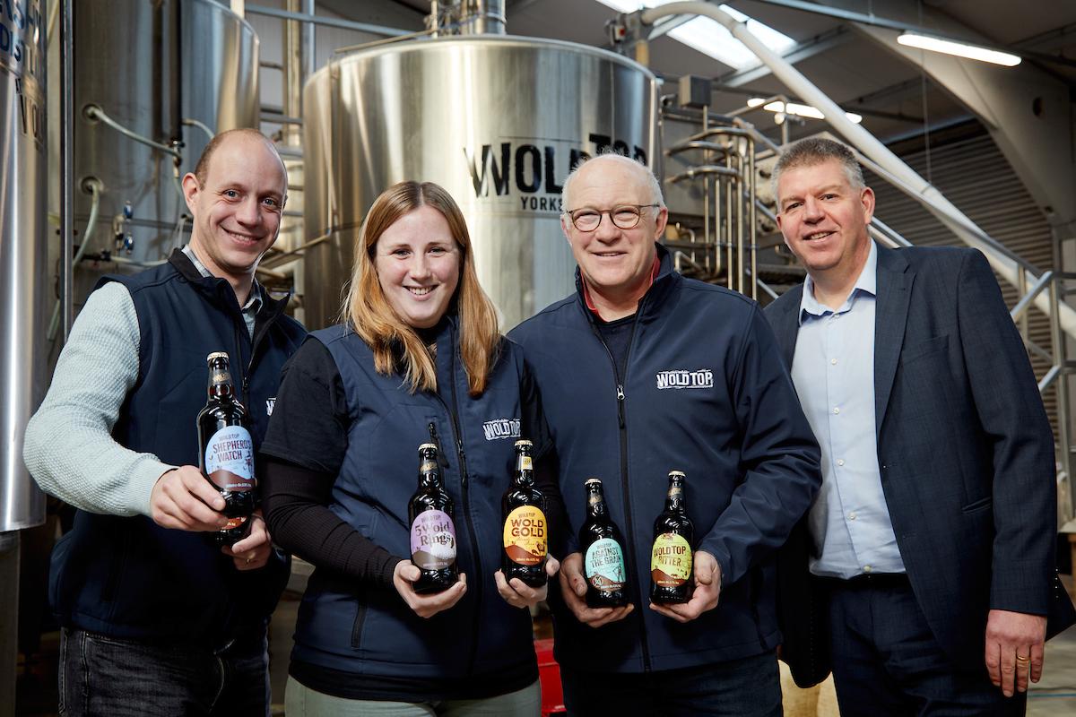 A group of Wold Top Brewery Colleagues holding beer bottles in their Brewery