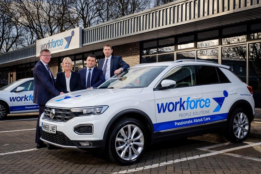 A group of colleagues standing behind a Workforce car and in front of the Workforce office