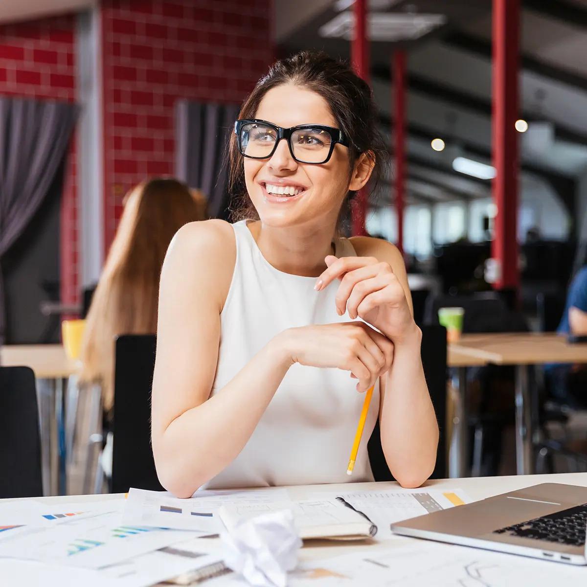 Female staff member sitting at a table looking at a laptop smiling.