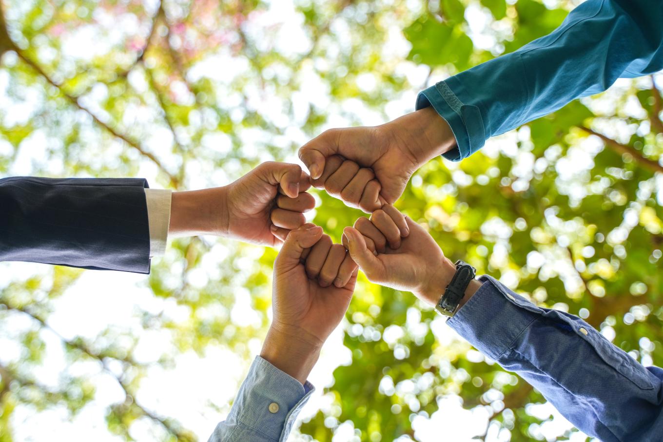 A group of four people fist bumping, view from the ground looking upwards