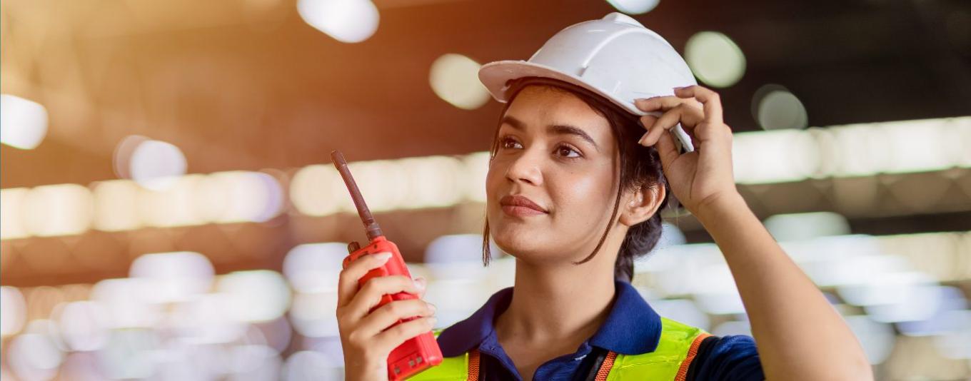 A female worker wearing a hard hat and speaking on a walkie talkie