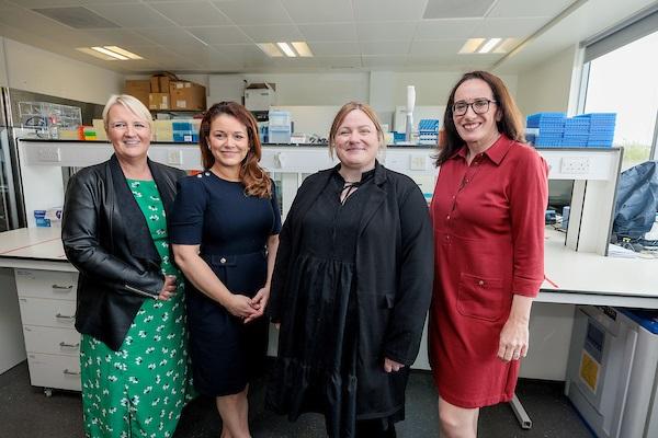 Four women standing in a laboratory setting, posing for a photo