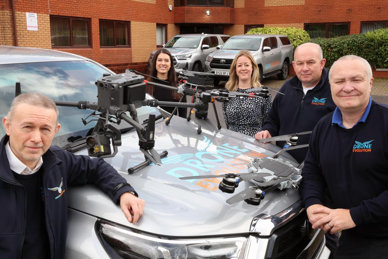 Photo of Drone Evolution staff with Ruby Godrich from Foresight and Bethan Bannister from British Business Bank standing outside with three drones sitting on top of a commercial vehicle